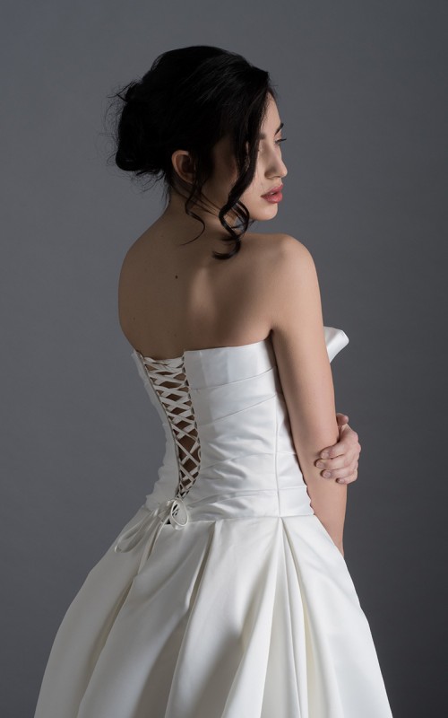 Bride wearing the Letizia strapless ball gown wedding dress in ivory duchess satin with corset lace-up back, handmade in London